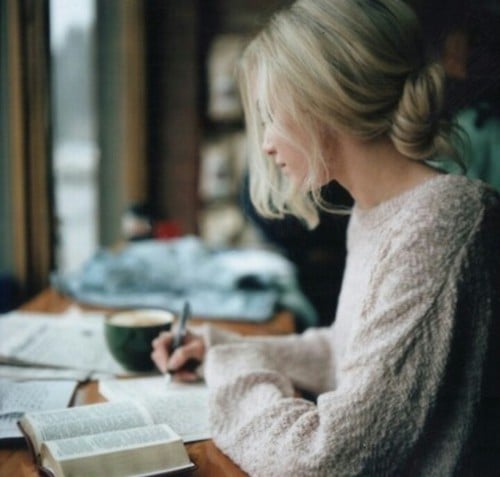 mujer con libros en una mesa escribiendo en una libreta 
