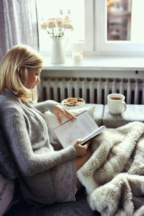 mujer sentada en un sillón al lado de la ventana leyendo y bebiendo café