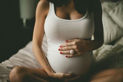 mujer embarazada sentada en la cama tocando su vientre 