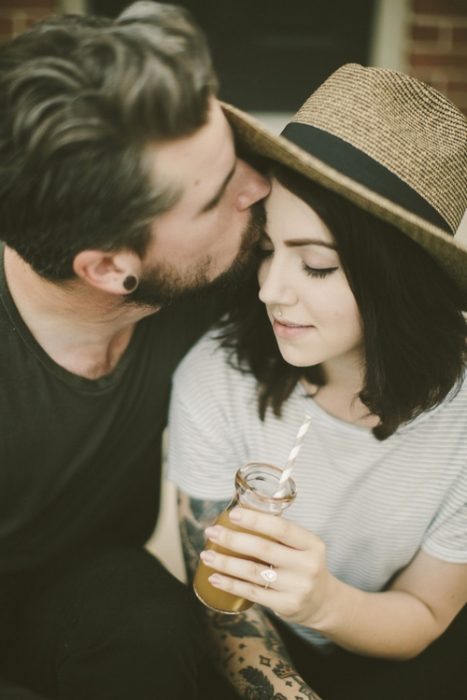 Hombre hipster besando a su novia en la frente 