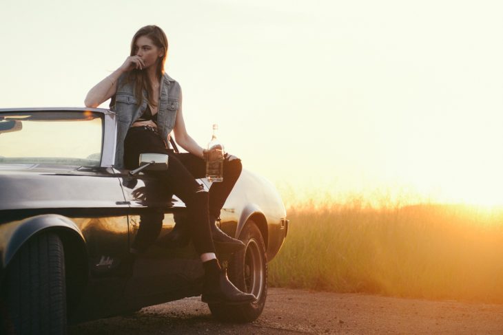 mujer femenina pero ruda en un carro a través de una puesta de sol 