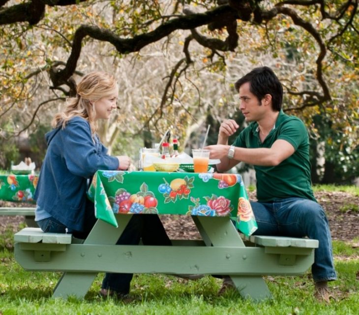 Pareja de novios al aire libre sentados a la mesa comiendo y viéndose frente a frente 