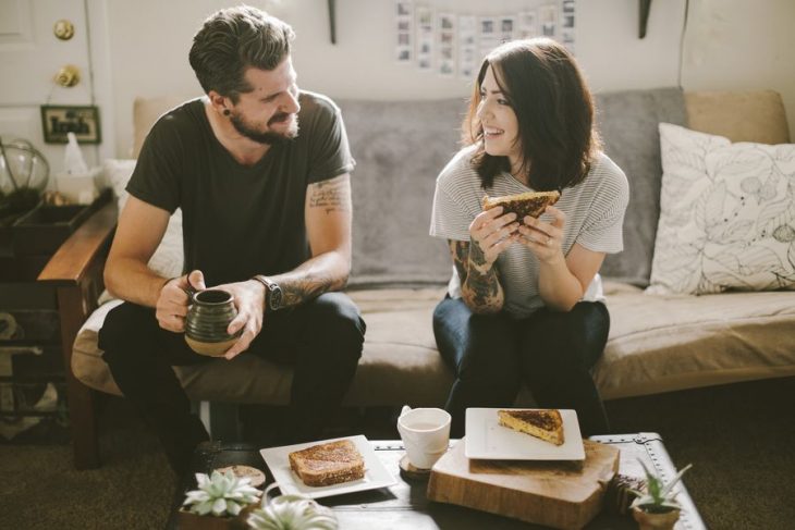 Pareja con tatuajes comiendo en un sofá 