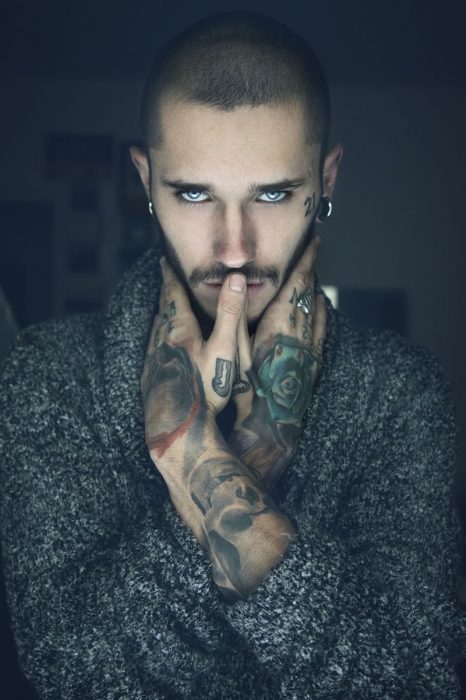 hombre de ojos azules con tatuajes y un aire misterioso