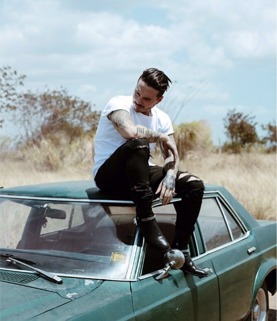 Hombre hipster con tatuajes arriba del techo de un carro