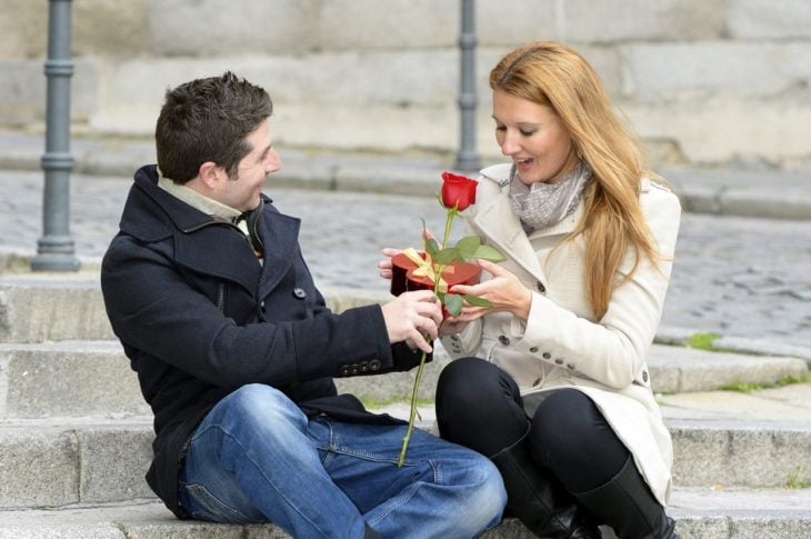Hombre sentado junto a su novia y entregándole una rosa roja 