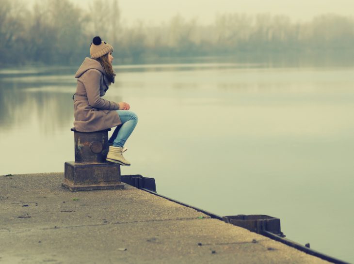 Mujer sentada a la orilla de un lago reflexionando 