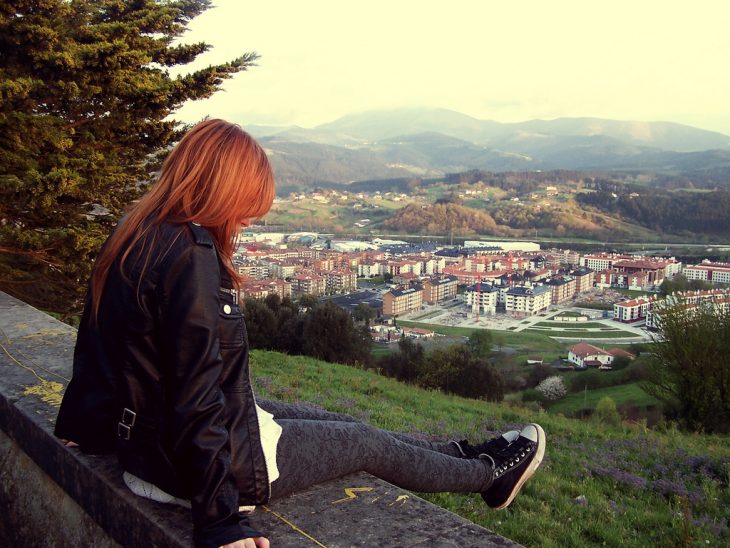 Chica de cabello rojo sentada en un parque observando la ciudad 