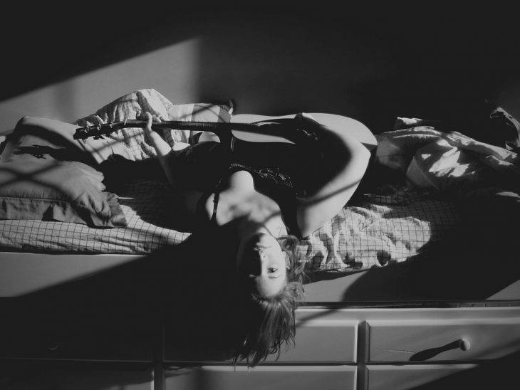 Foto en blanco y negro de chica con guitarra en la cama 