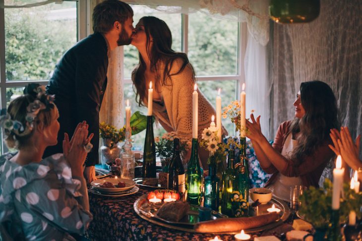 Novios besándose a la luz de la velas mientras les aplauden 