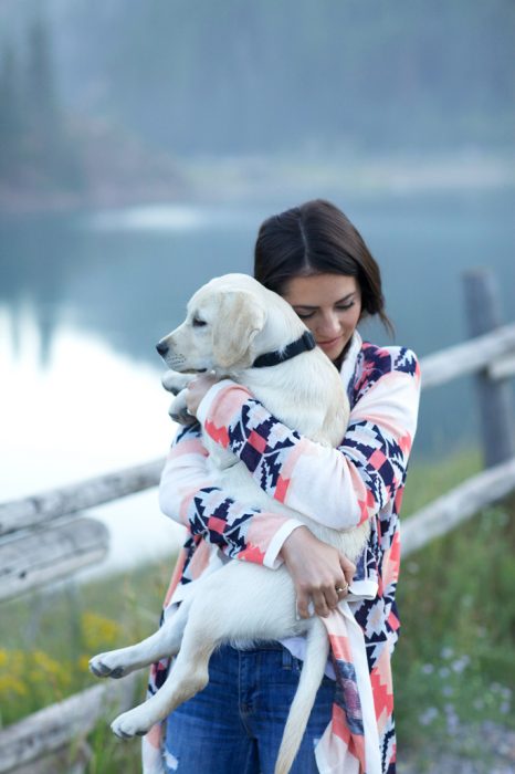 chica cargando a su perro a la orilla de un lago