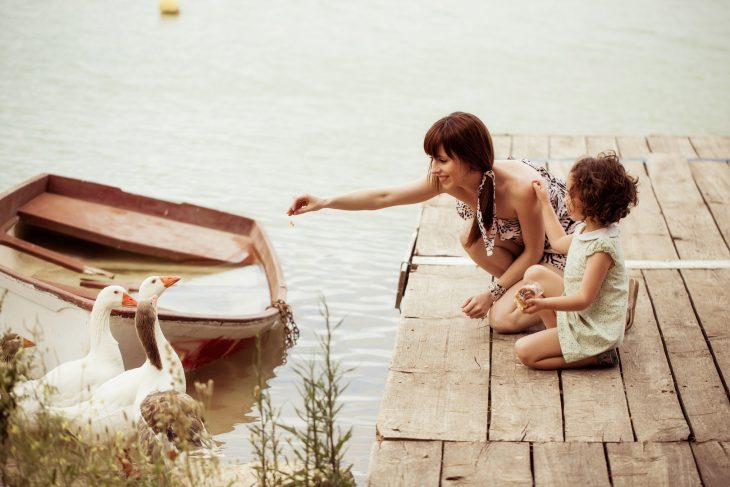 mama e hija alimentan un pato en el lago