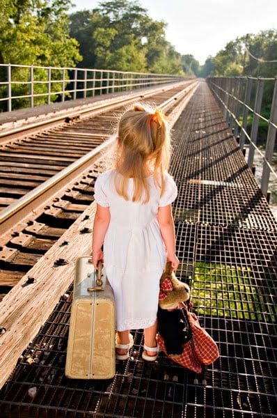 niña con una maleta en las manos caminando a un lado de las vías del tren 