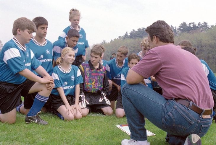 hombre reunido con un grupo de niños enseñándoles a jugar fútbol 