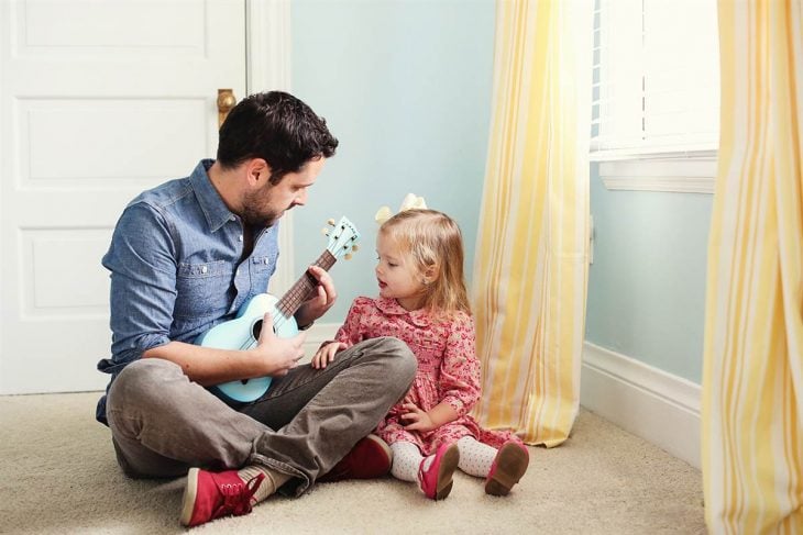 papá enseñando a su hija a tocar la guitarra 
