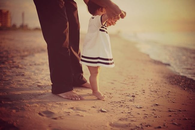 papa tomando de las manos a su hija mientras están en la playa 