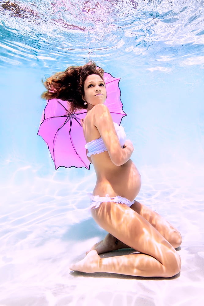 mujer con una sombrilla embarazada bajo el agua