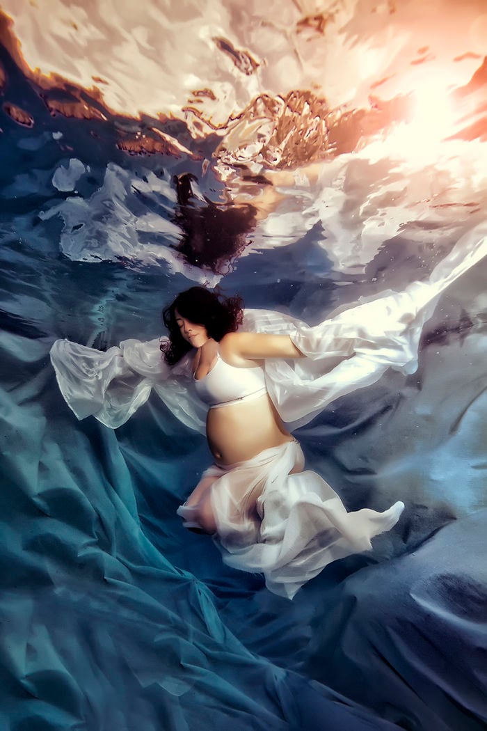 embarazada usando un vestido blanco y abriendo los brazos bajo el agua