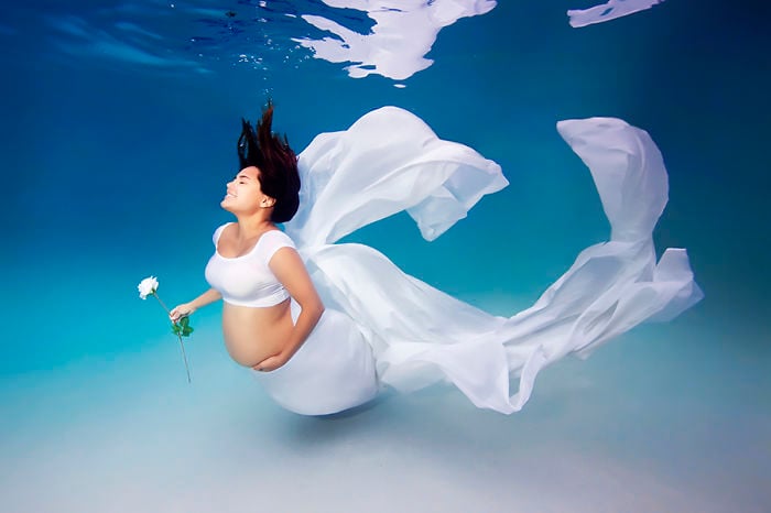 mujer vestida de blanco embarazada sosteniendo una flor bajo el agua 