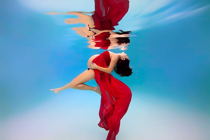 embarazada vestida de rojo tocándose el vientre tomándose una foto bajo el agua 