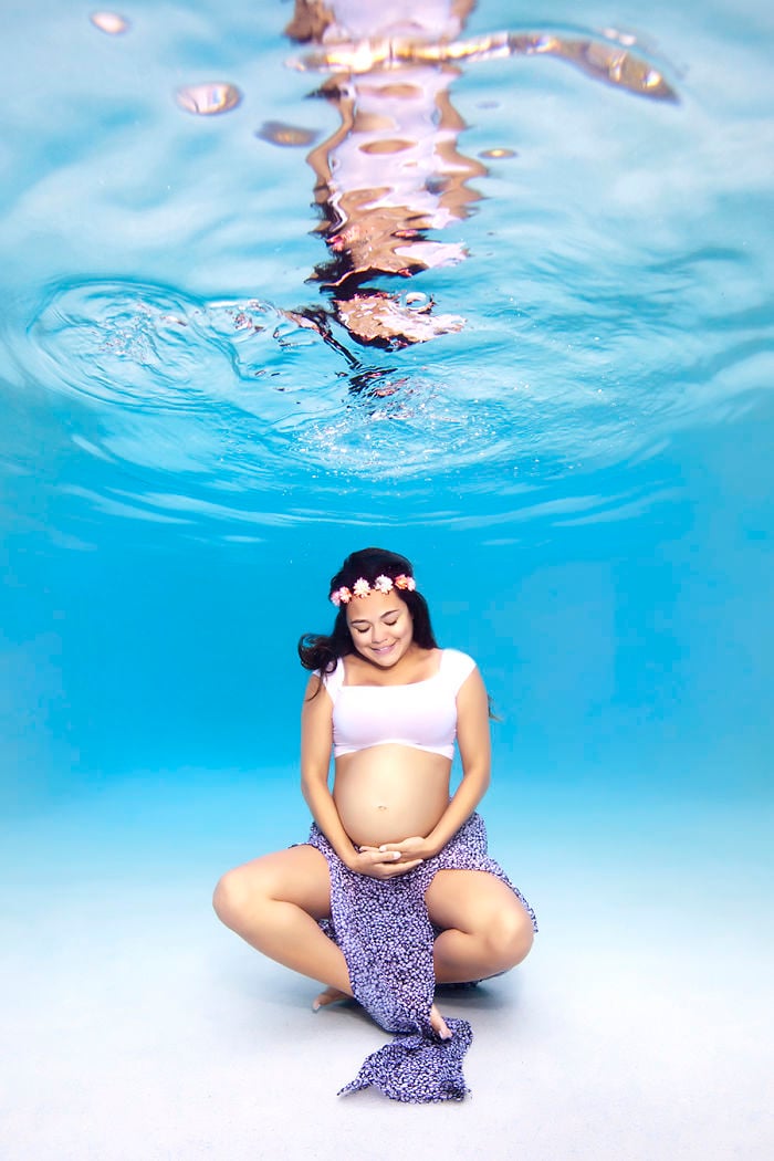 mujer usando una corona de flores top blanco y falda morada embarazada bajo el agua 