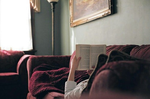 chica acostada en un sofá leyendo un libro 