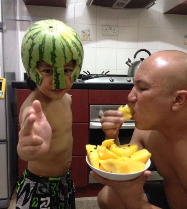 niño con una sandia como casco y padre comiéndose el resto de la fruta en un plato 