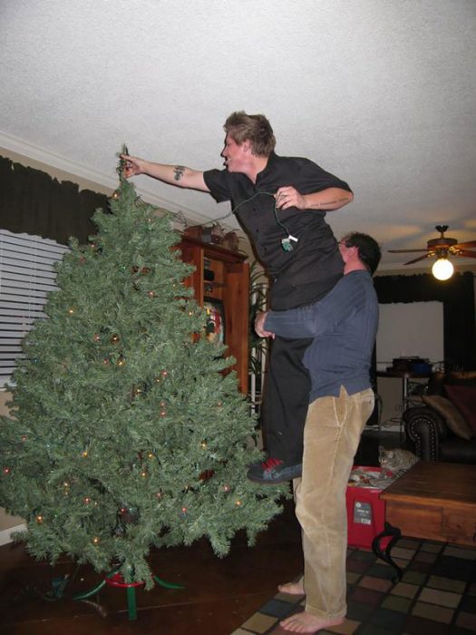 hombre cargando a otro para que coloque una estrella en la punta de un árbol de navidad 