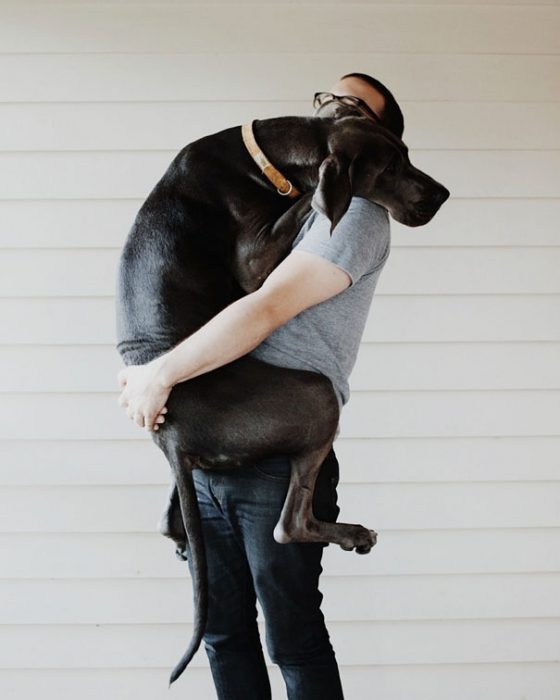 hombre cargando a un perro grande y negro en brazos 