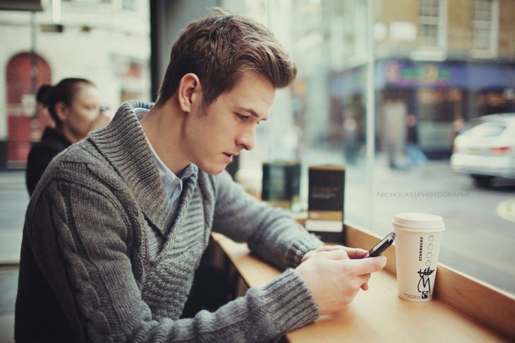 Chico tomando café y enviando un mensaje de texto 