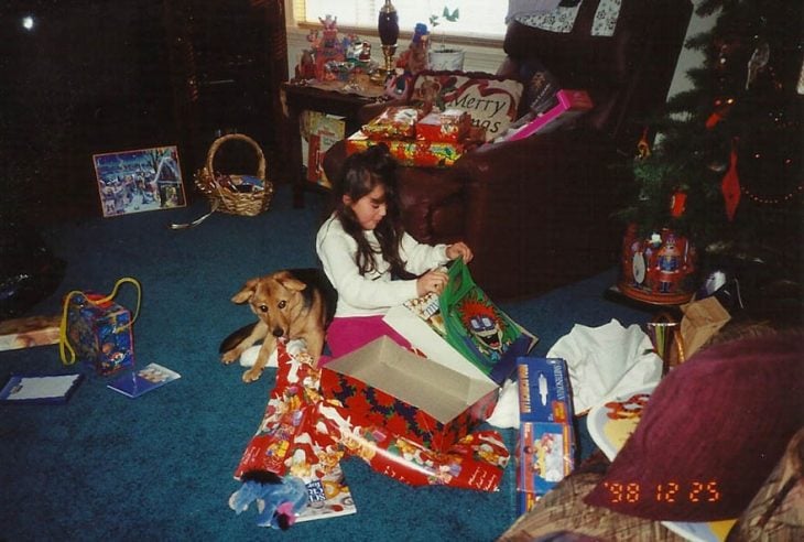 Niña abriendo regalos de navidad con un perro a su lado 