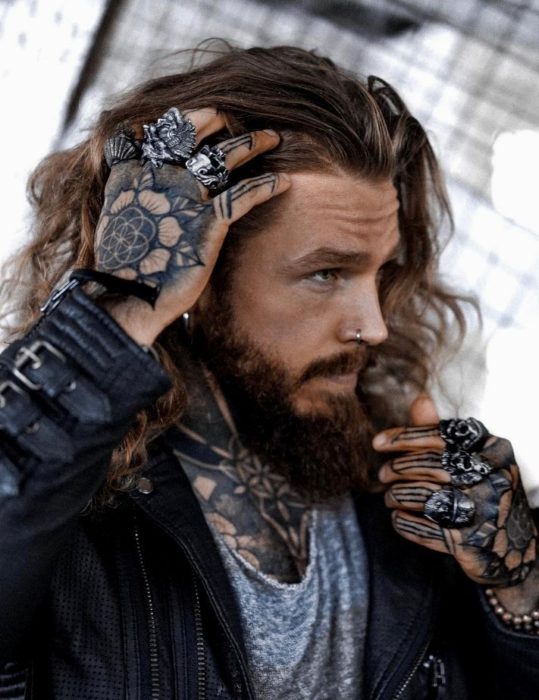 Hombre de cabello largo, barba y tatuajes en las manos