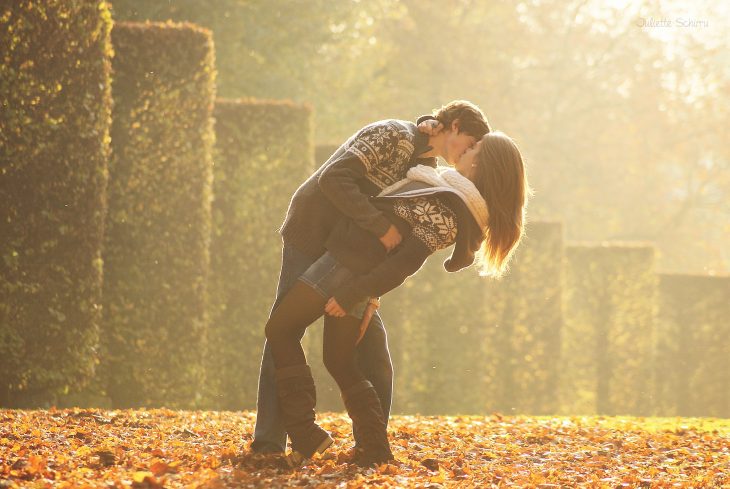 Pareja besándose sobre unas hojas de árbol secas 