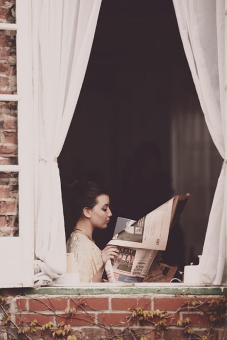 chica leyendo el periódico en una ventana 