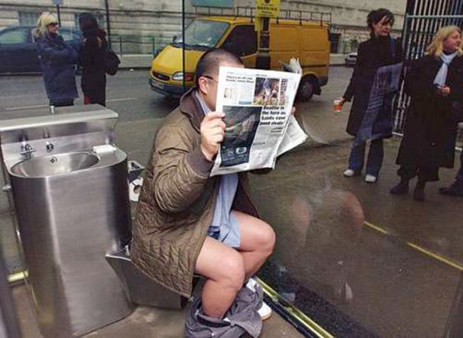 hombre leyendo un periódico sentado en un baño 