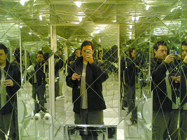 hombre tomandose una foto en un baño que esta hecho de espejos 