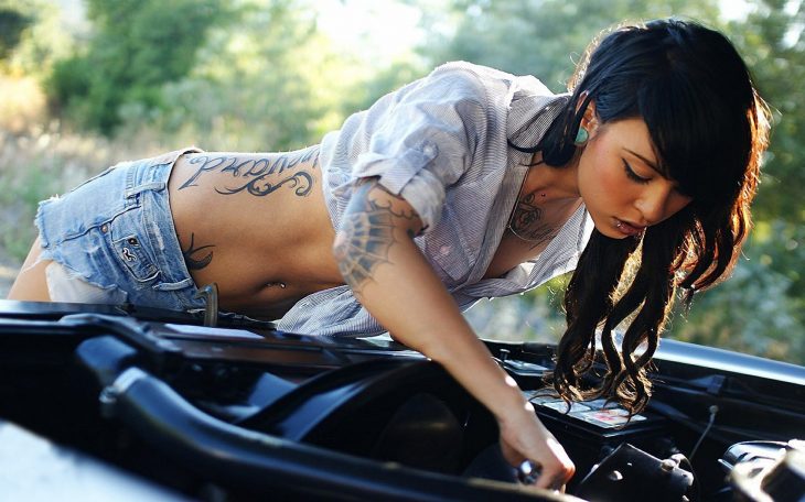 Chica con tatuajes arreglando un carro 