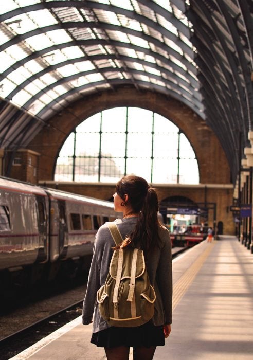 mujer con una mochila en los hombros parada en una estación de tren 