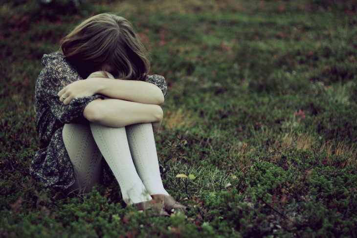 mujer sentada en el pasto abrazando sus rodillas y llorando 