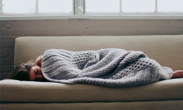 mujer recostada en el sofá durmiendo cubierta con una manta 