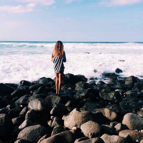 chica parada en unas rocas admirando el mar 