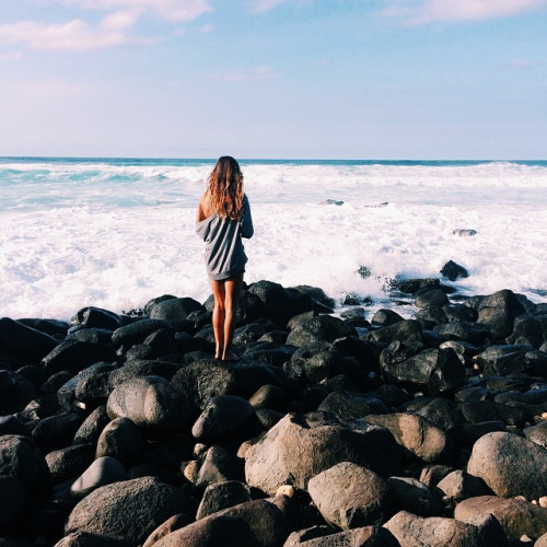 chica parada en unas rocas admirando el mar 