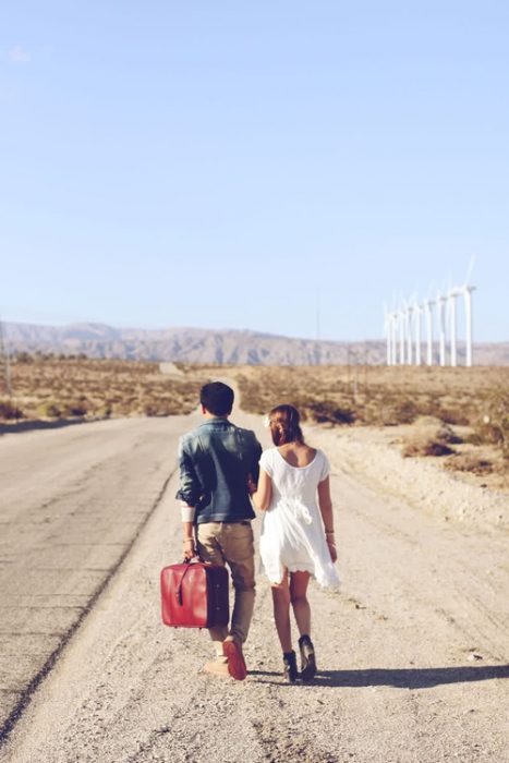 novios caminando a un lado de la carretera cargando una maleta 