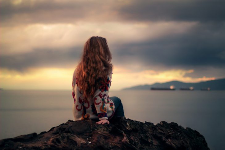 Chica sentada en una piedra viendo al mar 