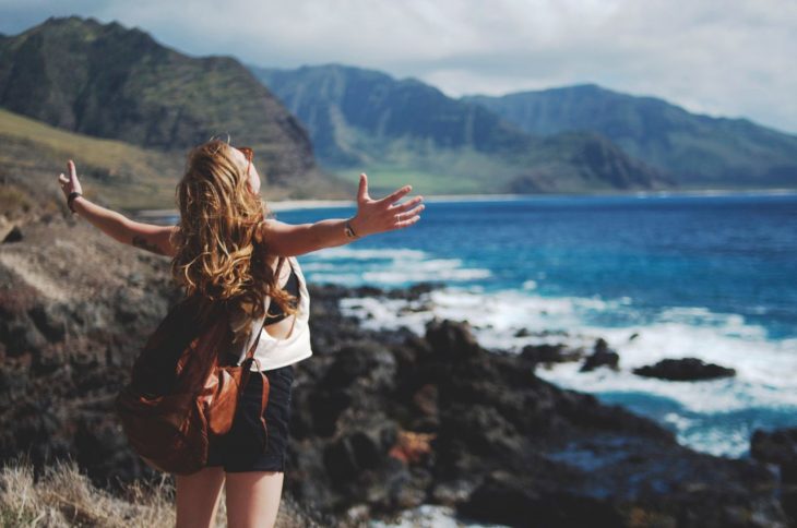 Chica al filo de la montaña con vista al mar y los brazos abiertos 