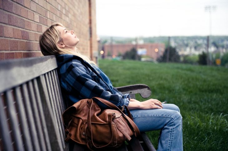 escena de la película blue valentine donde la protagonista esta sentada en una banca fumando y viendo hacia le cielo