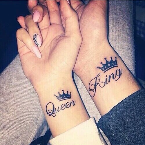 Pareja mostrando sus tatuajes en la muñeca del brazo que dicen rey y reina y sobre ellos una corona 