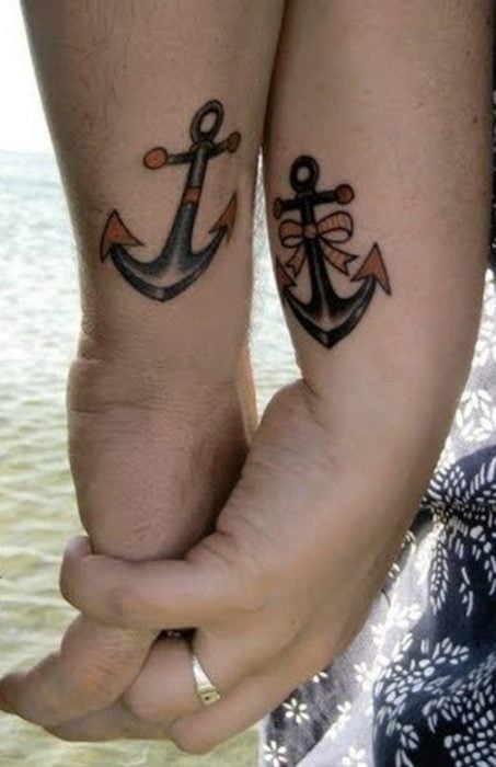 Manos entrelazadas de una pareja mostrando sus tatuajes en forma de ancla 