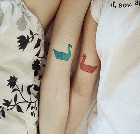 Pareja recostados en una cama mostrando sus tatuajes en forma de pájaros de papel de origami 