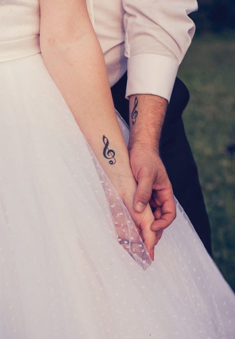 Pareja el día de su boda mostrando sus tatuajes en el brazo en forma de clave de sol